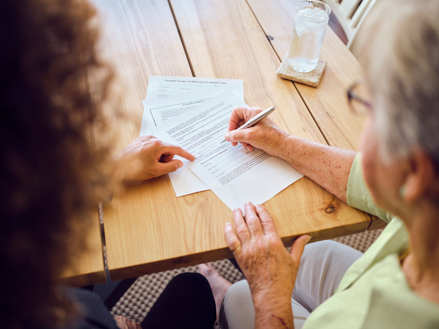 Elderly lady dressed in green signing a document with an estate planning lawyer in McAllen